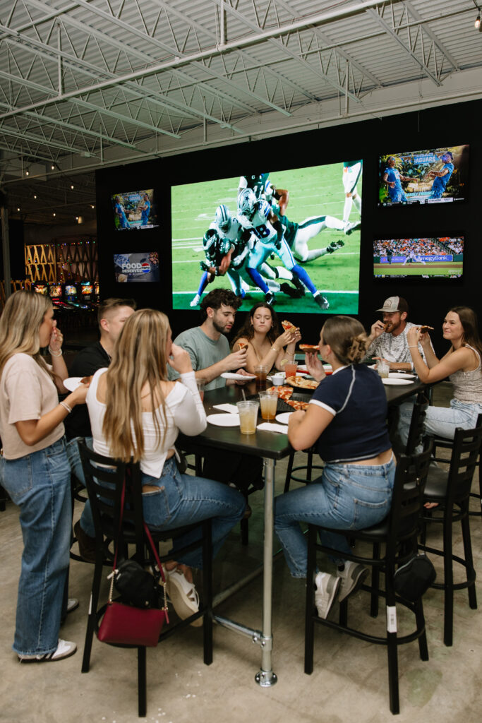 Guests chatting at tables near the big screens at Rec Hall in St. Charles, Missouri, where good pool etiquette keeps a shared bar space friendly